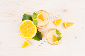 Freshly blended orange citrus smoothie in glass jars with straw, mint leaf,  cut orange, top view. White wooden board background, copy space.