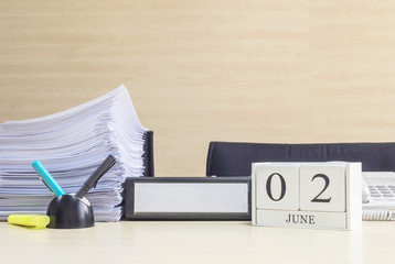 Closeup white wooden calendar with black 2 june word on blurred brown wood desk and wood wall textured background in office room view with copy space , selective focus at the calendar