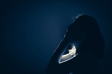 silhouette of depress woman standing in the dark with light shine behind, white tone