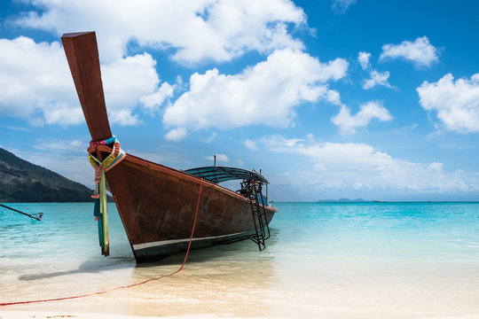 View of a wooden, long tail boat in the foreground on a beach in