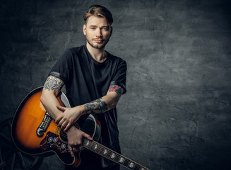 Handsome young acoustic guitar blues player with tattoos on arms.