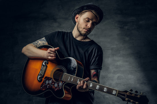 Handsome young acoustic guitar blues player with tattoos on arms.