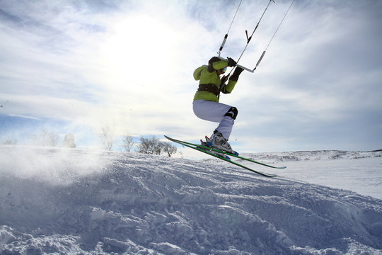 Snowkite rider jumping over hills flying high with kite and ski with snow splash, blue sky with clouds and snowy mountains background, extreme sports, hobby and recreation, fun and active life style