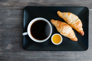 Traditional breakfast in France - cup of black hot steaming coffee, fresh hot croissants, honey.