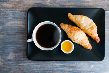 Traditional breakfast in France - cup of black hot steaming coffee, fresh hot croissants, honey.