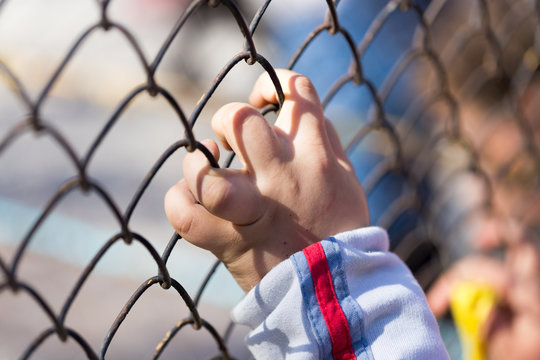 Child's hand on a grid of a metal fence