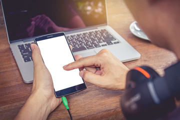 A man hand holding smart phone and use laptop computer on wood d