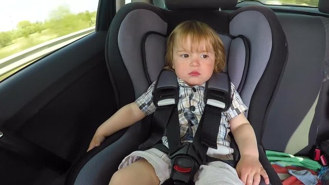Boy baby kid in a plaid shirt in the children's car seat in the car rides. Little baby child infant an automobile armchair. Time lapse