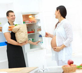 Happy pregnant woman and her husband cook food in the kitchen.