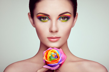 Portrait of beautiful young woman with rainbow rose. Bright colors. Long eyelashes, vivid colorful...