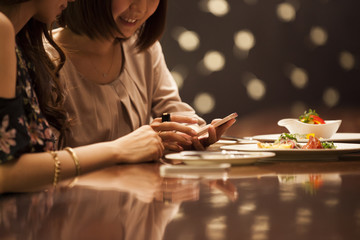 Women are laughing at the bar watching smartphone