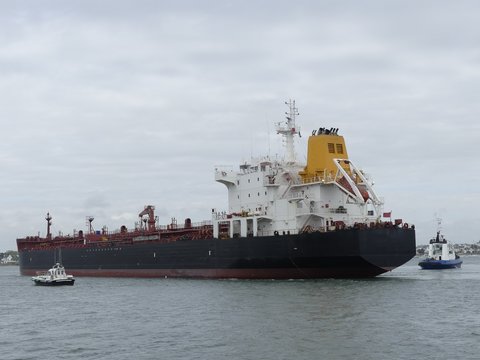 Products tanker ship maneuvering in the harbor with blue tugboat on stern. Horizontal  three-quarter stern view
