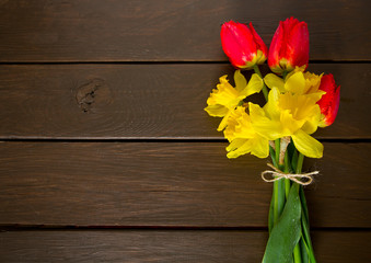 yellow daffodils and red tulips on dark wooden surface