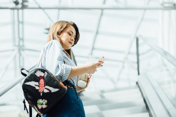 Series photo of gorgeous young woman holding disposable cup and smart phone in shopping mall