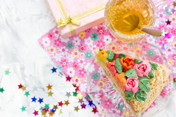 Piece of birthday cake, tea in cup, gift box and colorful confetti