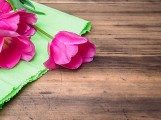 Pink tulips, floral arrangement on wooden background with green paper and space for message. Background for Mother's Day, 8 March and other greeting cards or invitations for lovely women. Soft focus.