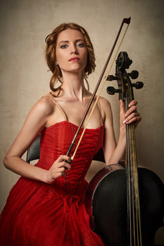 Female ballet dancer in red dress and pointe playing on antique black cello