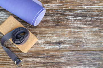 Accessories or props for yoga, pilates or fitness. Exercise lilac mat, two cork blocks and grey strap on wooden background.Copy space. - obrazy, fototapety, plakaty