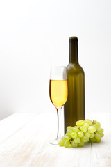 brush of green grapes, a bottle and glass on white