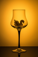 Object photo: a delicate glass on a high stem on an orange background. The glass inside has the silhouette of a Swan.background.