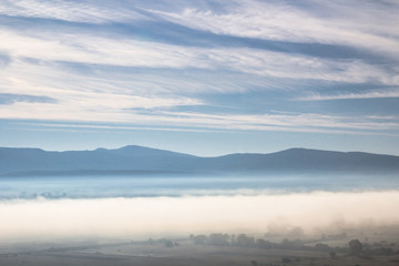 Beautiful morning atmosphere in a valley surrounded by hills with a magic mist full of bright light and white cloud and blue sky