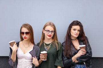 Three girls stand with cup of coffee near wall