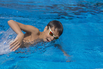 Child athlete swimming free style close up. Blue water background.