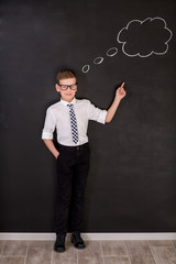 Handsome school boy in googles white shirt tie standing close to school desk with thinking cloud above the head.