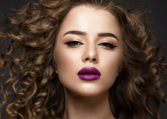 Beautiful brunette girl in move with a perfectly curly hair, and classic make-up. Beauty face. Picture taken in the studio on grey background.