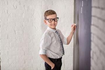 Obraz premium Handsome school boy in googles white shirt tie standing close to school desk with piece of chock.