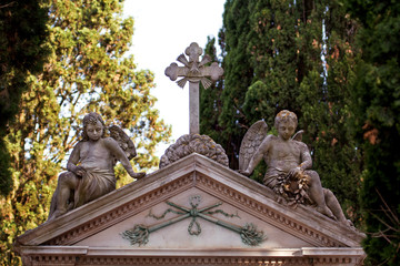 Obraz premium Part of masonic motives on the grave with children angels statues, monument in cemetery, close up. Old city cemetery with tombstones statues. Sculpture art.
