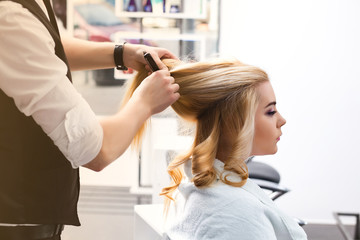 handsome Hairdresser does a hairstyle for a blonde girl in a beauty salon