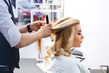 handsome Hairdresser does a hairstyle for a blonde girl in a beauty salon