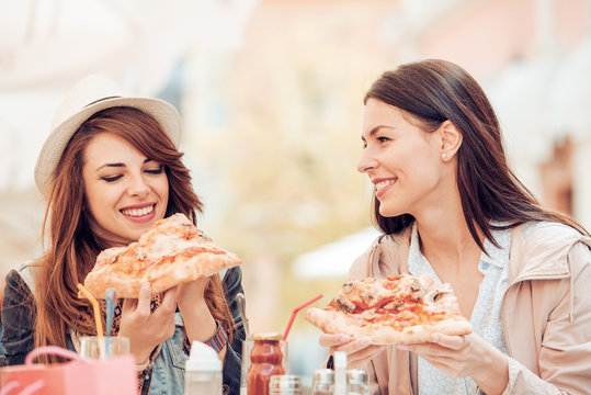 Portrait of two young women eating pizza outdoors