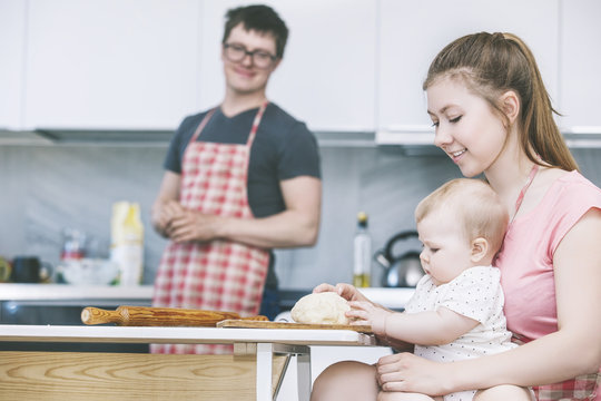 Mom, dad and little baby cooking cakes in the kitchen together and smiling