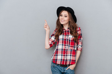 Cheerful girl in plaid shirt pointing finger up at copyspace