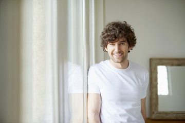 Confident young man portrait. Shot of happy young man standing in living room at the window. 