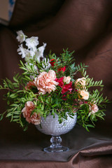 Asymmetric bouquet of roses, carnations, delphinium and hydrangeas on a brown background