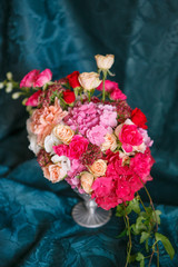 An asymmetric bouquet in a vase of roses, carnations and hydrangeas on a dark blue background
