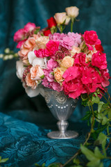 An asymmetric bouquet in a vase of roses, carnations and hydrangeas on a dark blue background
