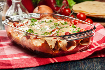Traditional mexican enchiladas with chicken meat, spicy tomato sauce and cheese in heat resistant dish