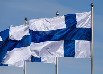 Three Finnish flags flying on sunny spring evening with blue sky in the background