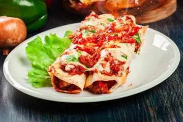 Traditional mexican enchiladas with chicken meat, spicy tomato sauce and cheese on a plate