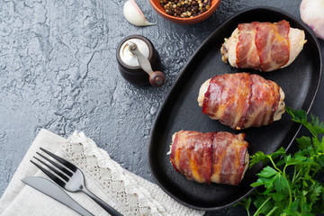 Baked chicken breast wrapped in bacon on a cast-iron frying pan on a black background. Selective...