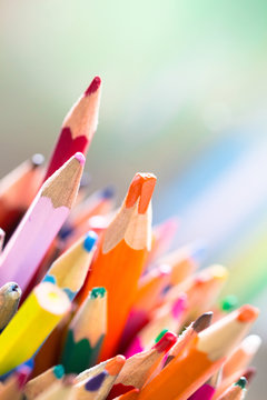 Stack of different color wooden pencil with orange color stand out on a bright green background as diversity concept