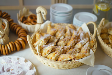Fresh pastries in a wicker basket and crockery on a table in a cafe, closeup.
