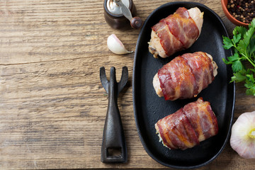 Baked chicken breast wrapped in bacon on a cast-iron frying pan on an old wooden  background. Selective focus. Top view. Copy space.