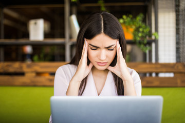 Young businesswoman suffering from headache in front of laptop at office