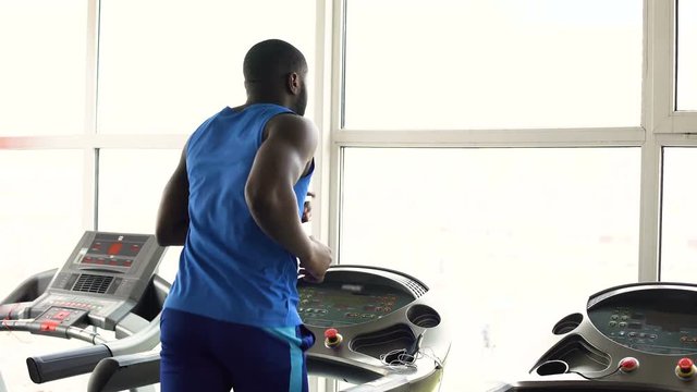 Muscular Afro-American man running on treadmill in the gym, workout, sport