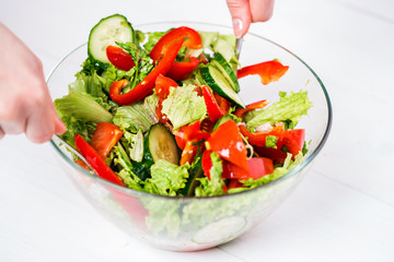 Young woman dressing vegetable salad with olive oil on a white background